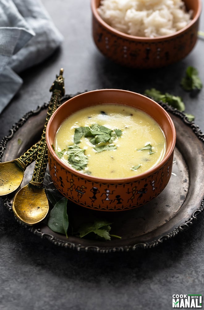gujarati kadhi served in a ceramic bowl and garnished with cilantro with another bowl of rice in the background