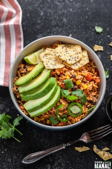 bowl filled with rice, beans and topped with avocado slices, tortilla chips, cilantro and jalapeño