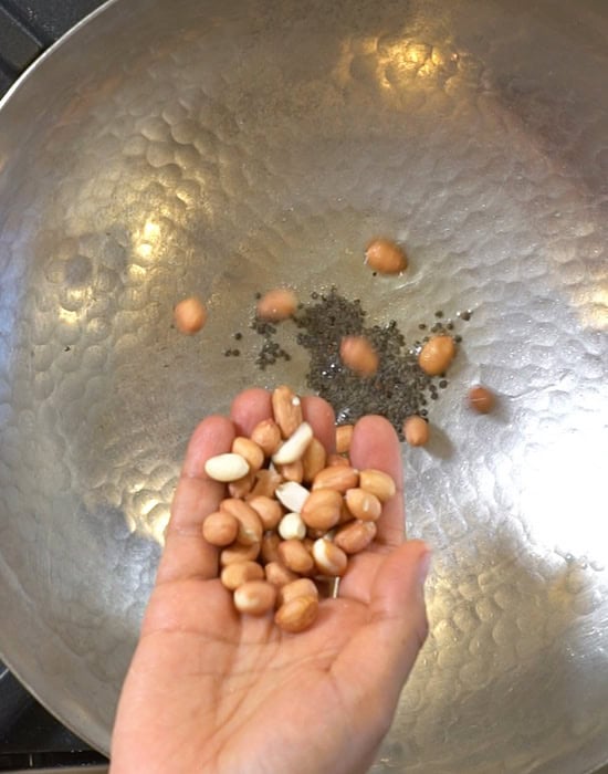 a hand adding some raw peanuts to a kadai