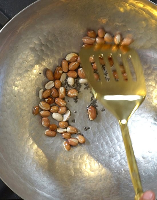 a golden spatula stirring peanuts in a kadai