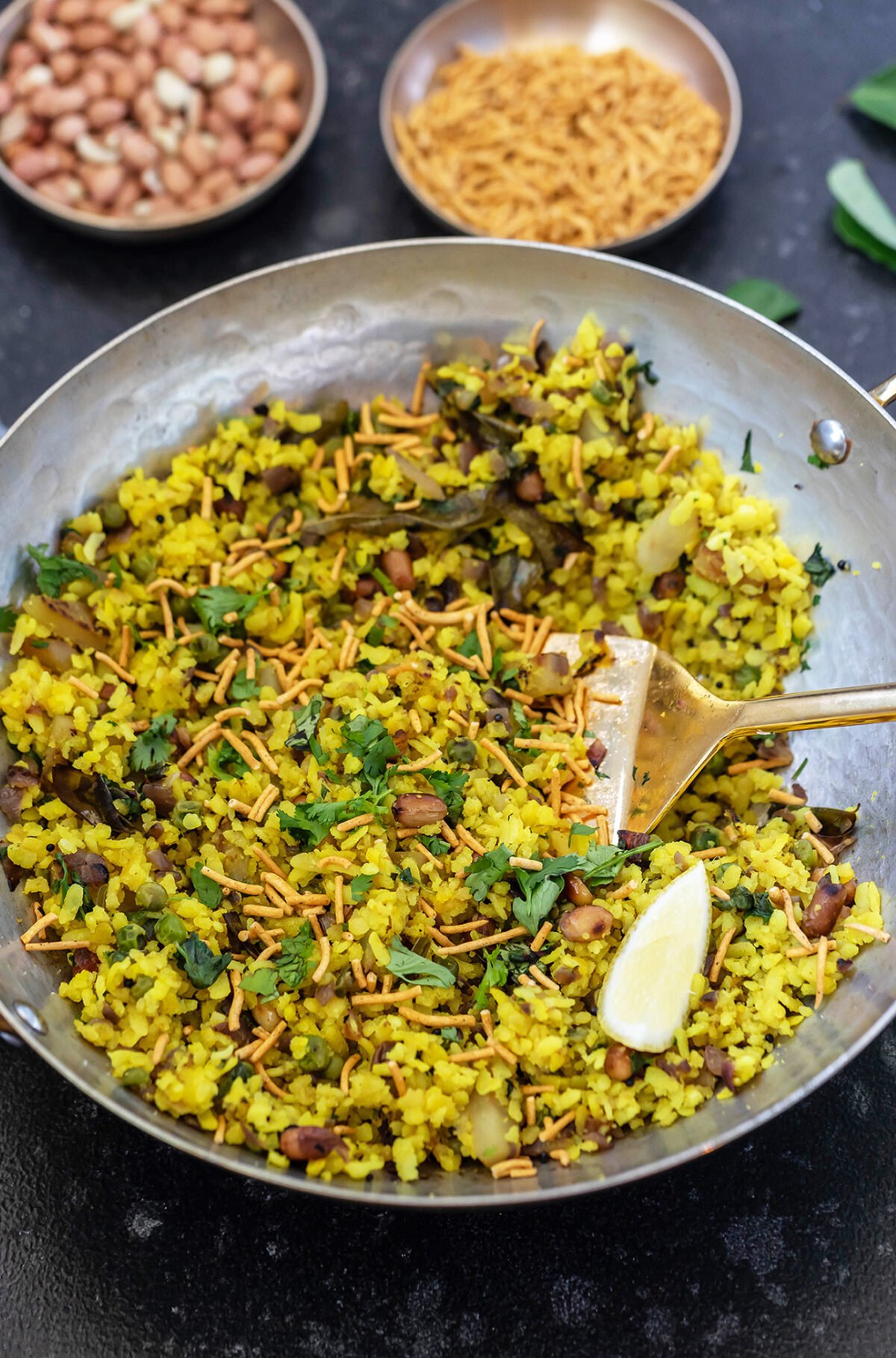 poha served in a copper kadai with sev on top and lemon wedge placed on side