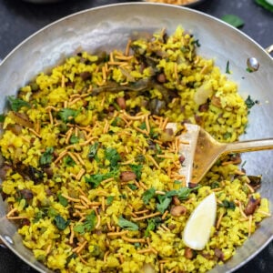 poha served in a copper kadai with sev on top and lemon wedge placed on side