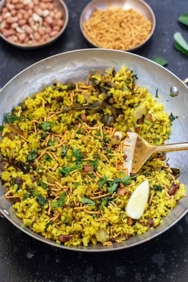 poha served in a copper kadai with sev on top and lemon wedge placed on side