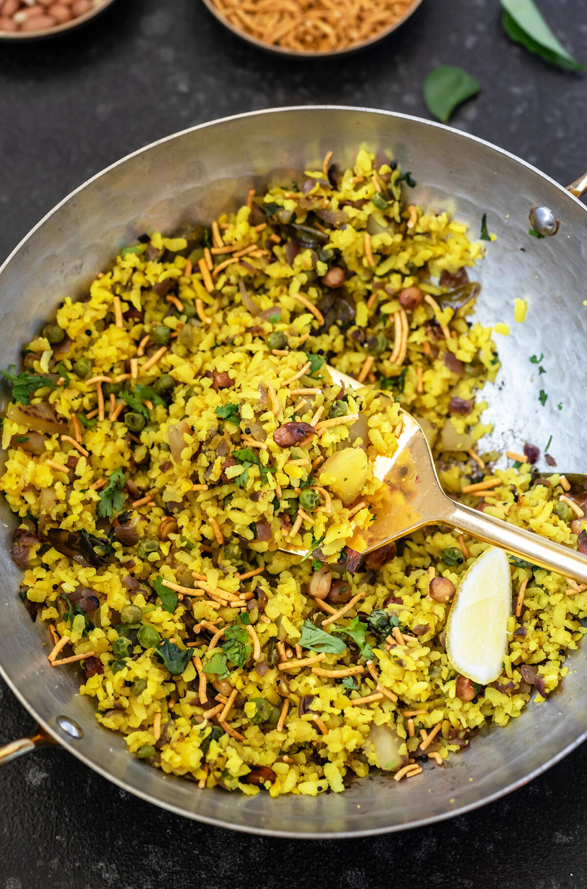 poha garnished with cilantro and bowls of peanuts and sev placed in the background