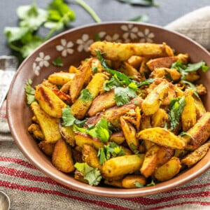 spiced arbi fry served in a brown bowl, garnished with cilantro and a twig of cilantro and curry leaves placed in the background