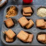 baked gur para arranged in muffin tray with a glass of milk placed in the back
