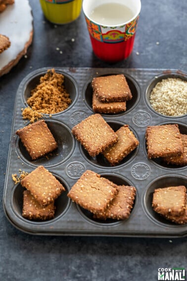 baked gur para arranged in muffin tray with a glass of milk placed in the back