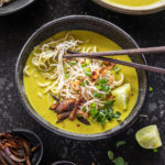 bowl of burmese khow suey with chopsticks and garnished with cilantro, lime wedge