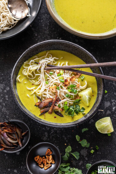 bowl of burmese khow suey with chopsticks and garnished with cilantro, lime wedge