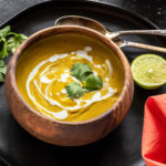 cauliflower lentil soup served in a round wooden bowl and garnished with cilantro with 2 spoons and a cut lime placed on the side
