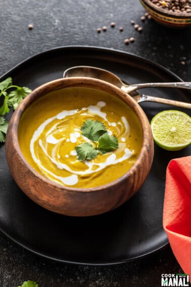 cauliflower lentil soup served in a round wooden bowl and garnished with cilantro with 2 spoons and a cut lime placed on the side