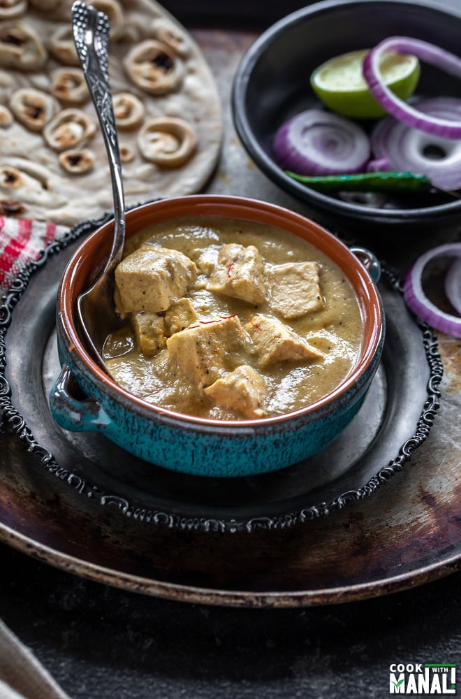 creamy shahi tofu curry served in a blue bowl with sliced red onion rings on one side and tandoori roti placed in the background