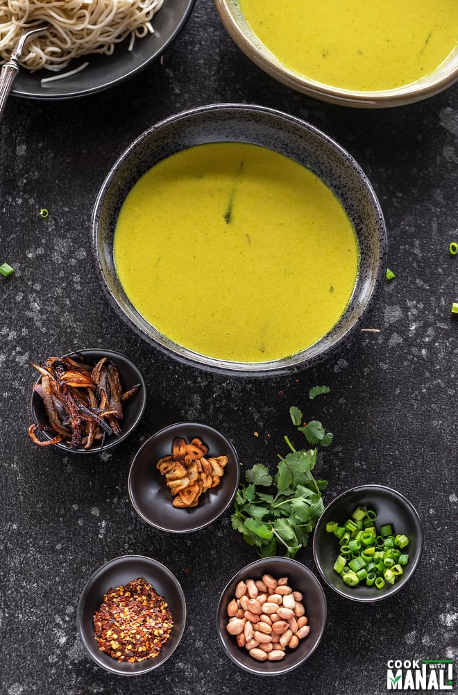 small bowls containing chopped cilantro, peanuts, green onions, fried garlic, fried onion and a large bowl of soup