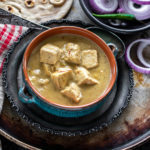 creamy shahi tofu curry served in a blue bowl with sliced red onion rings on one side and tandoori roti placed in the background