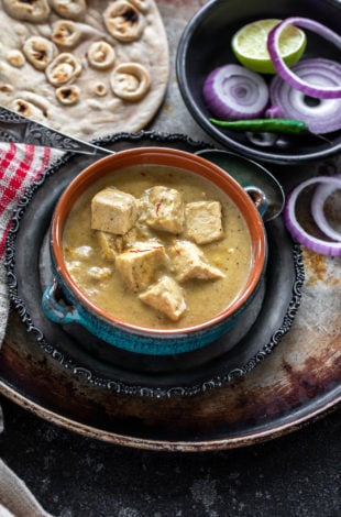 creamy shahi tofu curry served in a blue bowl with sliced red onion rings on one side and tandoori roti placed in the background