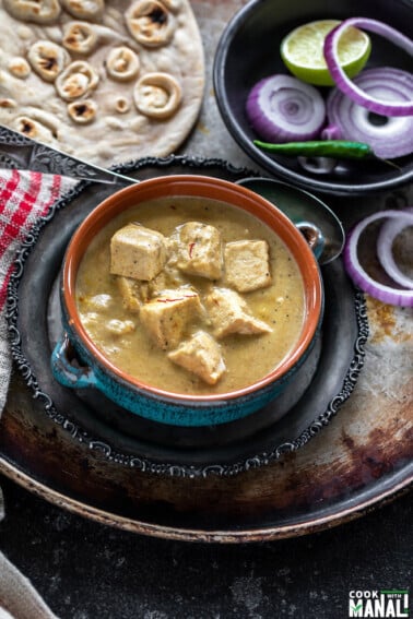 creamy shahi tofu curry served in a blue bowl with sliced red onion rings on one side and tandoori roti placed in the background