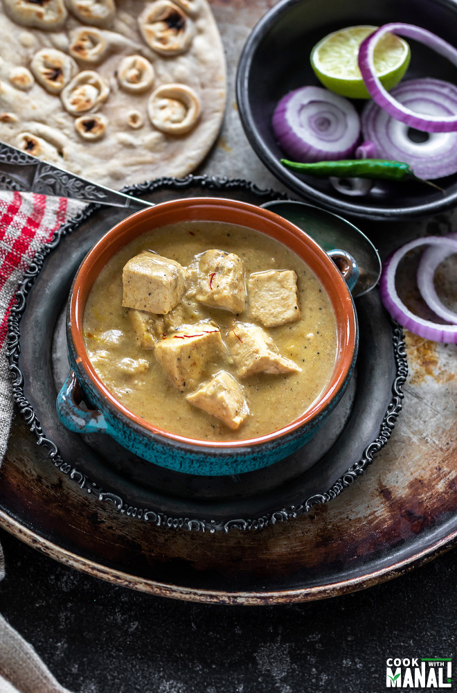 creamy shahi tofu curry served in a blue bowl with sliced red onion rings on one side and tandoori roti placed in the background
