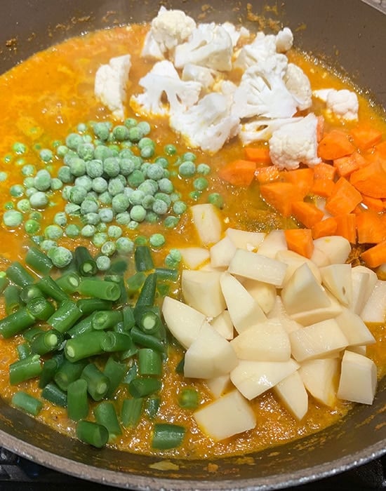 cubed potato, carrots, cauliflower, peas added to a pan