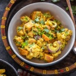 bowl of yellow color salad with cauliflower, sweet potato, onions and garnished with cilantro placed in a handcrafted serving tray