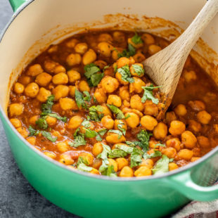chana masala in a green color pot with a wooden spatula