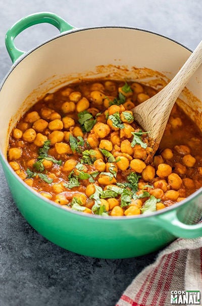 chana masala in a green pot with a wooden spatula