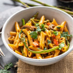 bowl of pasta with asparagus, peppers and topped with cilantro with few more asparagus placed in the background
