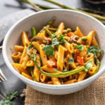 bowl of pasta with asparagus, peppers and topped with cilantro with few more asparagus placed in the background