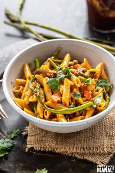 bowl of pasta with asparagus, peppers and topped with cilantro with few more asparagus placed in the background