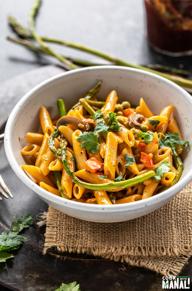 bowl of pasta with asparagus, peppers and topped with cilantro with few more asparagus placed in the background