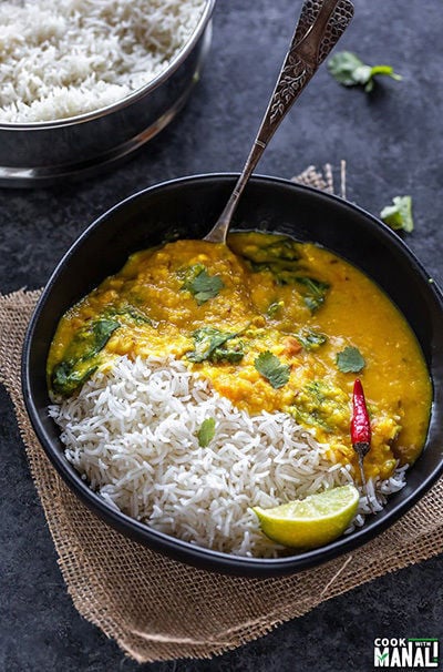 rice and dal in a black bowl, garnished with cilantro and a spoon placed on the side