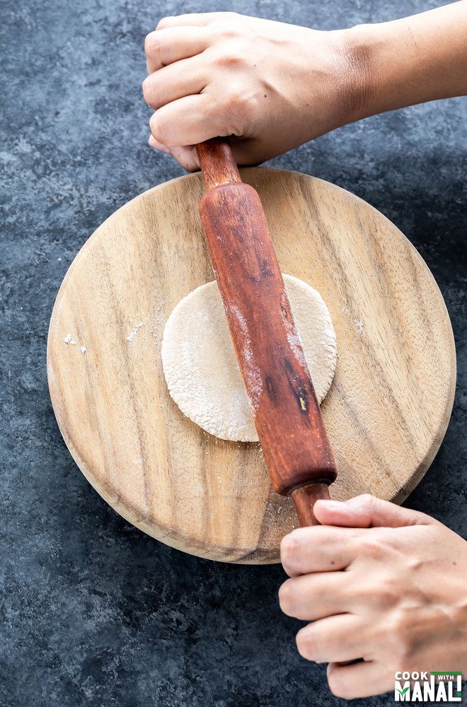 pair of hands rolling a flatbread on a board with a wooden rolling pin