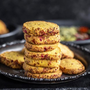 stack of thandai cookies arranged on a plate with spices placed in the background