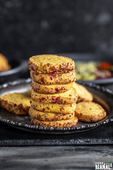 stack of thandai cookies arranged on a plate with spices placed in the background