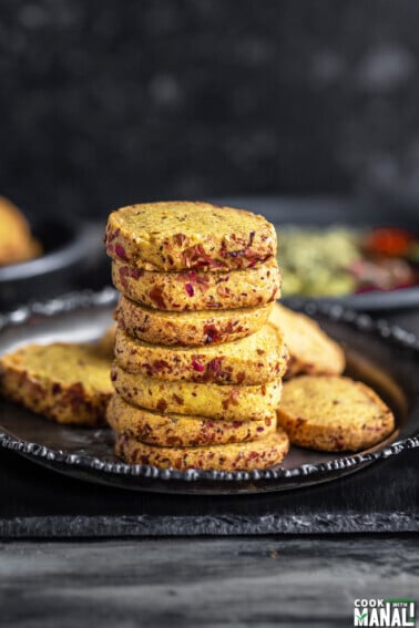 stack of thandai cookies arranged on a plate with spices placed in the background