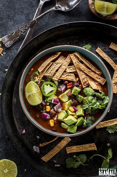 bowl of tortilla soup garnished with tortilla chips, cilantro, avocado, jalapeno