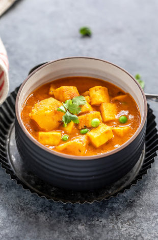 curry of potatoes, paneer and peas served in a black bowl and garnished with cilantro