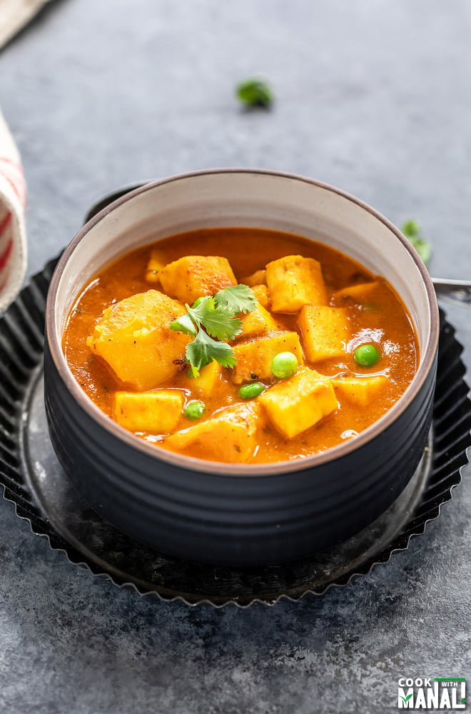 curry of potatoes, paneer and peas served in a black bowl and garnished with cilantro