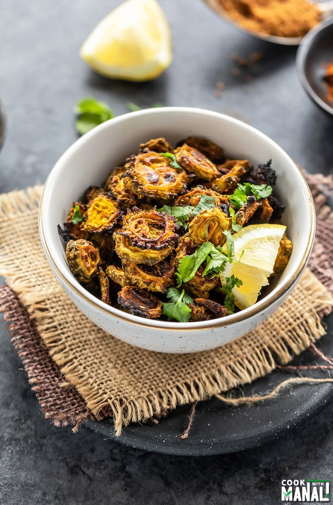 baked karela served in a white bowl, garnished with cilantro and lemon wedge