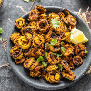 sliced karela with spices served in a black plate garnished with lemon wedge and cilantro