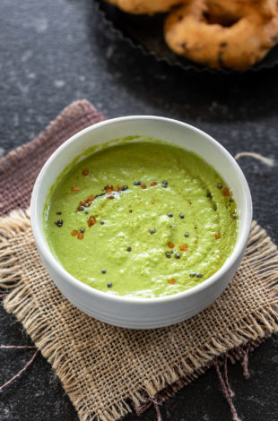 bowl of green color coconut chutney with few vadas placed in the background