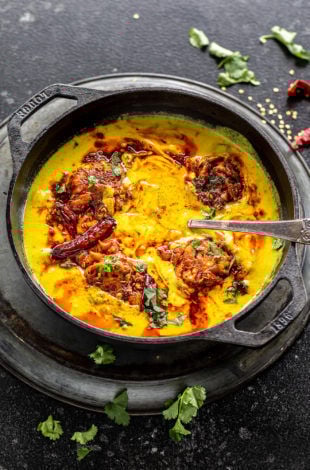 punjabi kadhi pakora served in a cast iron kadai with cilantro and broken red chilies scattered in the background