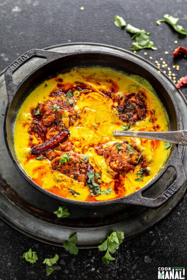 punjabi kadhi pakora served in a cast iron kadai with cilantro and broken red chilies scattered in the background