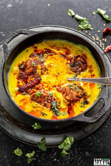 punjabi kadhi pakora served in a cast iron kadai with cilantro and broken red chilies scattered in the background