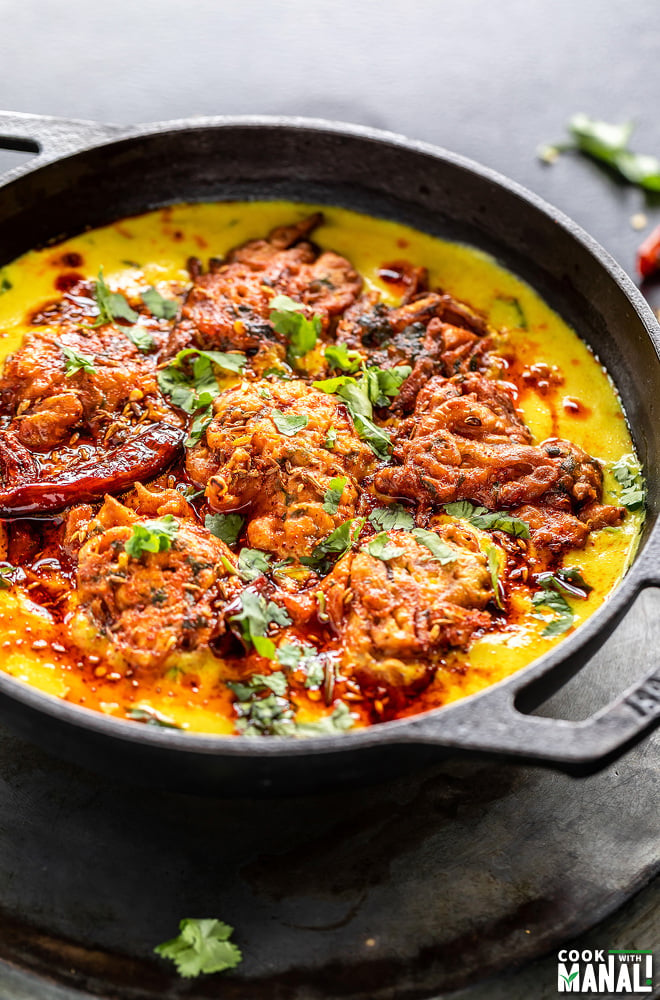 bowl of yellow kadhi with pakora in a iron kadai garnished with cilantro