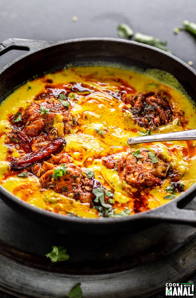 punjabi kadhi pakora served in a cast iron kadai with cilantro and broken red chilies scattered in the background