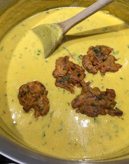kadhi with fried pakoras in a steel pot