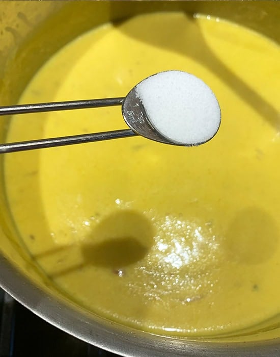 a spoon adding salt to boiling kadhi