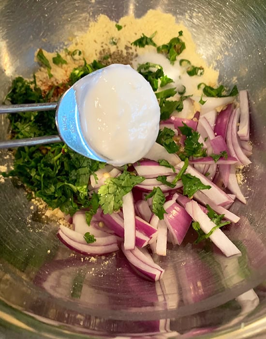 adding yogurt to sliced onion, chilies for making pakoras