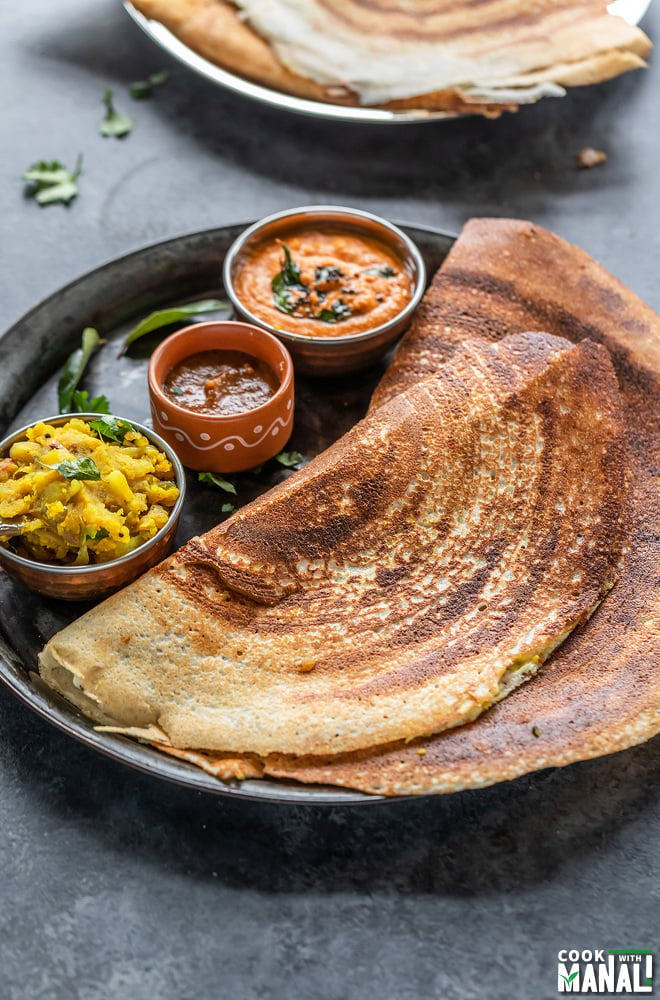 two dosa placed in a plate with bowls of chutneys and potato masala