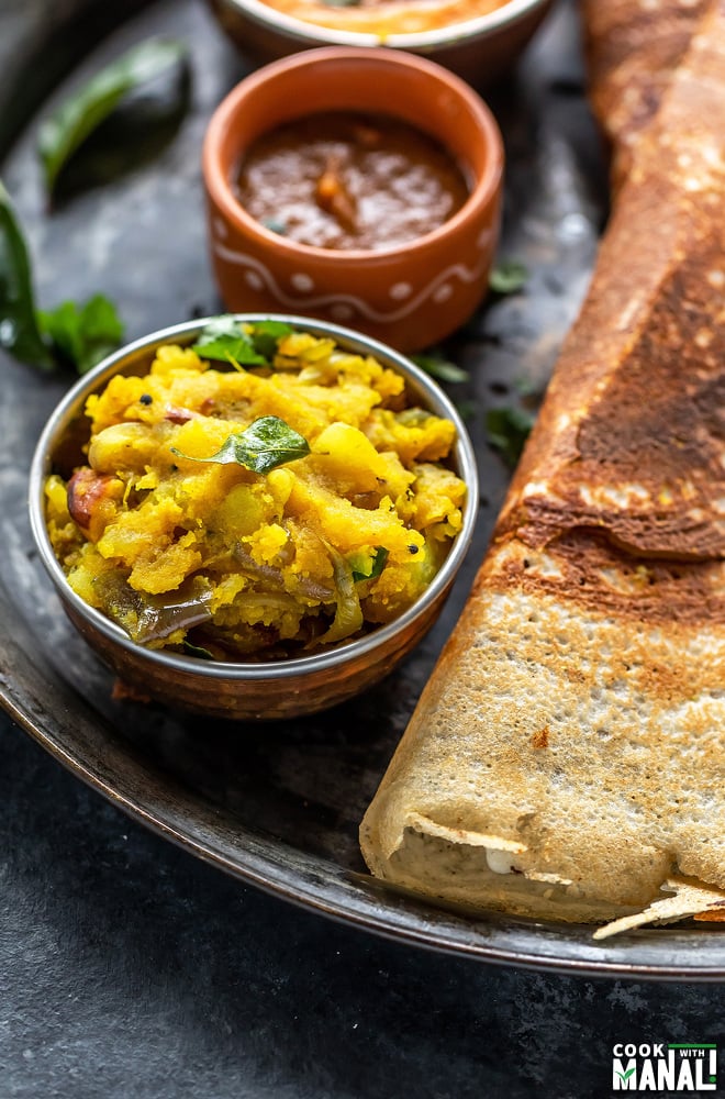 bowl of potato masala placed in a plate along with dosa on the side and more bowls in the background